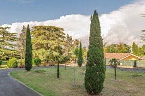 A landscaped area with neatly trimmed trees, a paved path, and a building with a tiled roof.