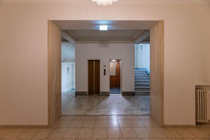 A hallway with a marble floor, wooden doors, and a staircase.