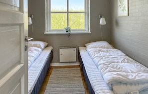 A small, clean room with two beds, a window with a view of greenery, a wall-mounted air conditioner, and a door with a key lock. - Lovely home in Hvide Sande with sauna (Hvide Sande)