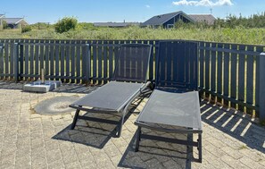A sunlit outdoor seating area with two lounge chairs and a table, enclosed by a wooden fence. - Lovely home in Hvide Sande with sauna (Hvide Sande)