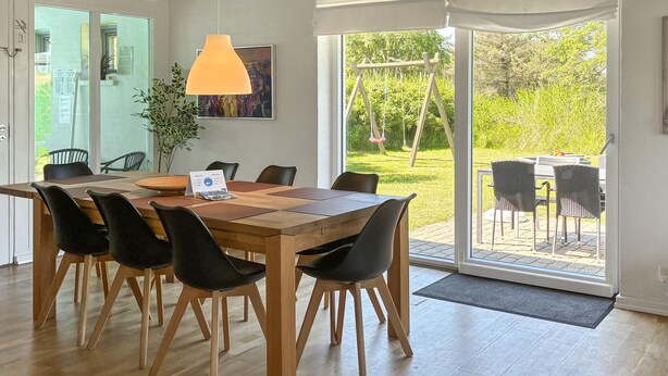 A dining area with a wooden table and chairs, a pendant light, and a view of a garden through a glass door. - Lovely home in Hvide Sande with sauna (Hvide Sande)