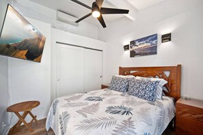 Ein Schlafzimmer mit einem Bett, einem Deckenventilator, einem an der Wand montierten Fernseher und Kunstwerken.