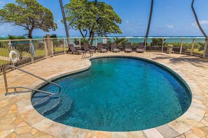 Ein Pool mit Blick aufs Meer, umgeben von Liegestühlen und Palmen.