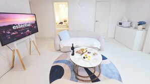 Un salon moderne équipé d’un téléviseur à écran plat, d’un canapé, d’une table basse avec de la nourriture et des boissons, d’un four à micro-ondes et d’un appareil de climatisation.