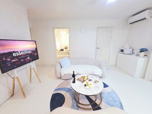 Ein modernes Wohnzimmer mit Fernseher, einer Couch, einem Couchtisch mit Speisen und Getränken, einer Mikrowelle und einer Klimaanlage.