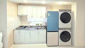 Une cuisine compacte avec des meubles blancs, un évier et deux machines à laver superposées.