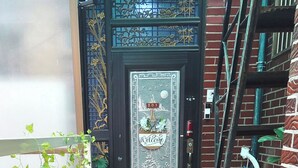Une porte noire ornée d’un panneau métallique décoratif, une pancarte indiquant « Bienvenue » et le numéro « 201 ».