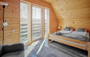 Ein Schlafzimmer mit einem Bett, einem Sessel, einer Lampe und Blick durch große Fenster.