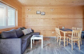 Ein gemütliches Blockhaus-Interieur mit einer Holzwand, einem grauen Sofa, einem kleinen weißen Tisch und einem Holzesstisch mit Stühlen.