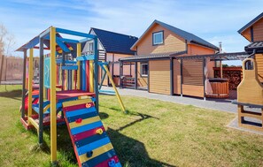 Ein Spielplatz mit Rutsche und Klettergerüst, ein Holzhaus mit Garage und eine überdachte Terrasse.