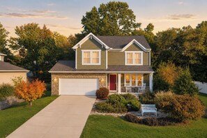 Ein zweistöckiges Haus mit Garage, einer Veranda mit Stühlen und einem gepflegten Rasen.