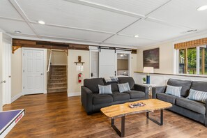 Un vaste espace de vie doté d’un plancher en bois, de deux canapés sombres ornés de coussins à rayures, d’une table basse et d’un escalier menant à une autre pièce.