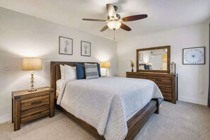 Ein Schlafzimmer mit Bett, Nachttischen, Deckenventilator, Kommode, Spiegel und Wandbildern.