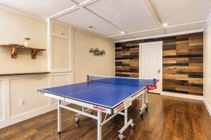 Ein Pingpongtisch in einem Raum mit Holzboden, einer weißen Tür und einer Wand mit rustikaler Holzvertäfelung.