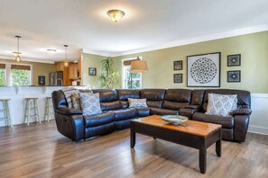 Ein Wohnzimmer mit einem ledernen Ecksofa, einem Holztisch und einer Küche im Hintergrund.
