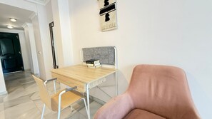 Ein Zimmer mit einem Holztisch, einem Stuhl, einem gepolsterten Sessel, einem grauen Kopfteil und einem an der Wand hängenden Kunstwerk.