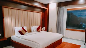 Ein modernes Hotelzimmer mit einem großen Bett, einem Holzkopfstück, einem Fenster mit Vorhängen und einem kleinen runden Tisch.