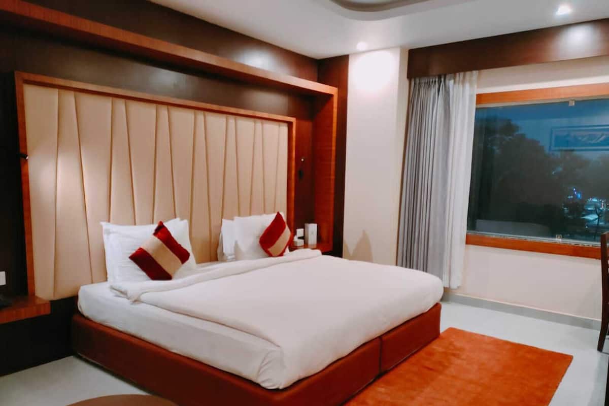 Una habitación de hotel moderna con una cama grande, cabecera de madera, una ventana con cortinas y una pequeña mesa redonda.
