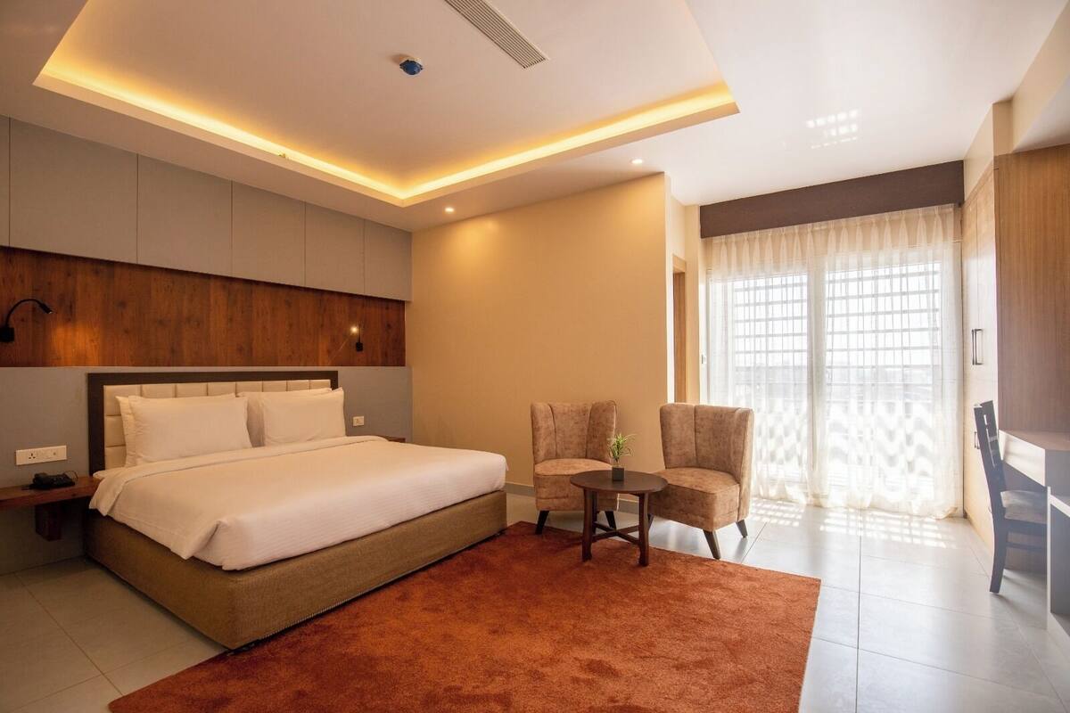 Un hotel moderno con una cama grande, un rincón de descanso, una mesita y vistas al exterior a través de un ventanal amplio.