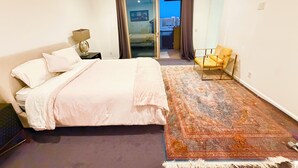 Een slaapkamer met een bed, nachtkastje, stoel, groot vloerkleed en uitzicht door een glazen deur.