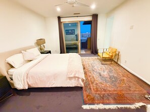 Ein Schlafzimmer mit Bett, Nachttisch, Stuhl, großem Teppich und Blick durch eine Glastür.
