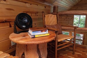 Interieur van een houten hutje met een ventilator, een stoel en een stapel boeken.