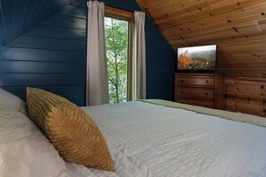 Een slaapkamer met een bed, een houten dressoir, een televisie en een raam met gordijnen.