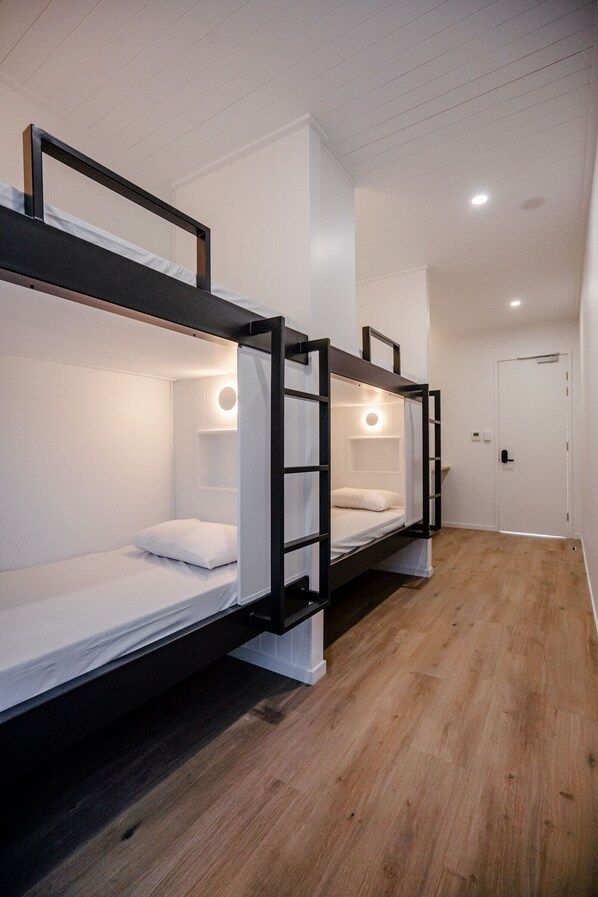 Une chambre avec un lit superposé, un plancher en bois, des murs blancs et une porte.