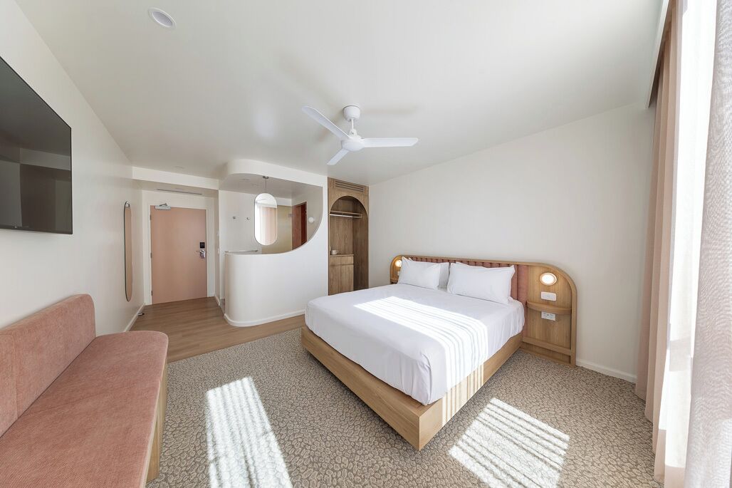 A hotel room with a bed, a sofa, a ceiling fan, and a view of the outside.