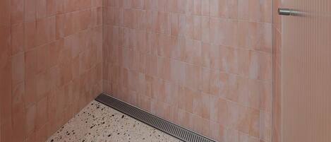 Une salle de bain avec des carreaux roses, une pomme de douche et trois bouteilles de shampoing accrochées au mur.