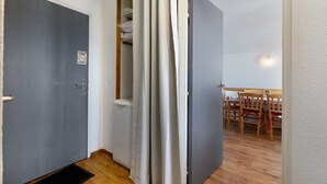 A room with a grey door, a white curtain, a wooden floor, and a dining table with chairs. - Apartment “Valmeinier Le Miras” with Mountain View, Private Terrace and Wi-Fi (Valmeinier)