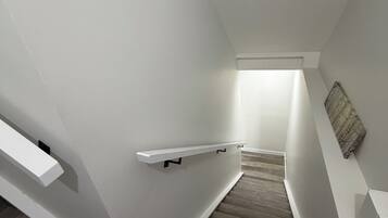 Een trap met houten treden en witte muren, die leidt naar een lichte kamer.
