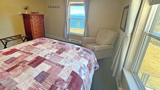 Une chambre à coucher comprenant un lit, une chaise, une commode et une fenêtre donnant sur la mer.