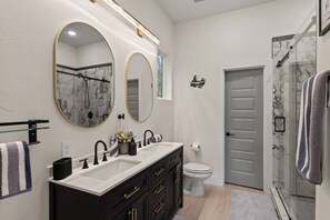 A modern bathroom with a double sink vanity, a toilet, a shower enclosure, and a door with a decorative fish decal. - New Construction | Lake View Retreat (Gun Barrel City)