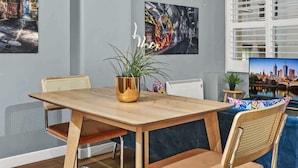 Un comedor con mesa de madera, dos sillas, una planta en maceta y decoración en la pared.