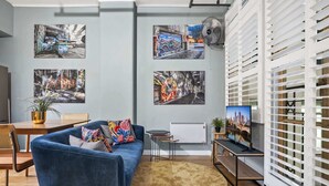 Un salón moderno con un sofá azul, un tapete redondo y cuadros que representan escenas urbanas.