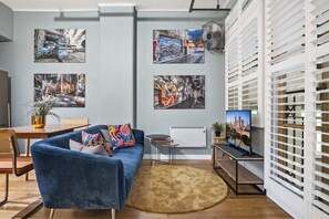 A modern living room with a blue sofa, a round rug, and wall art depicting urban scenes. - Temple Court Suite in Melbourne CBD (Melbourne)