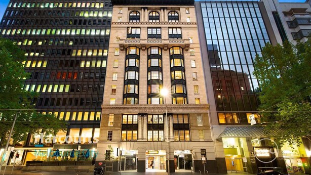Un edificio de varios pisos con un estilo arquitectónico clásico, que presenta una entrada central con ventanas amplias y una fachada decorativa.