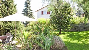 A garden with a variety of plants, a patio with a table and chairs, and a house in the background.