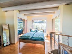 Een slaapkamer met een houten bed, uitzicht op het omliggende landschap, een balkon en een trap.