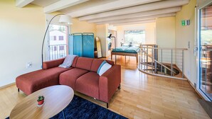 A modern living room with a red sofa, a small round table, and a blue rug. There is a staircase leading to an upper level.