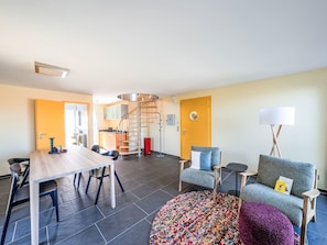 Een moderne woonkamer met een eethoek, een spiltrap en een bank met een lamp.