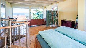 A bedroom with a bed, a desk, a chair, a window with a view, and a balcony.
