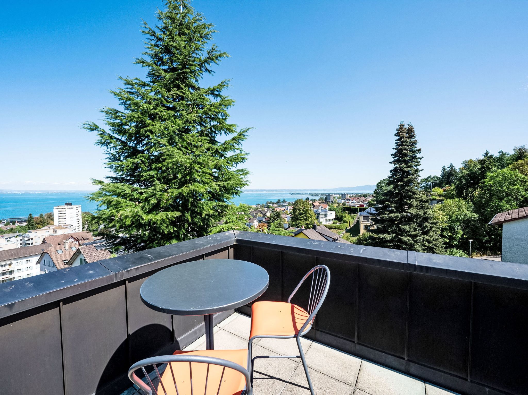 En balkon med bord og stole, med udsigt over bybillede og et vandareal.