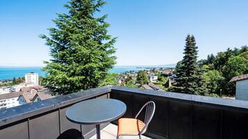 En balkon med bord og stole, med udsigt over bybillede og et vandareal.