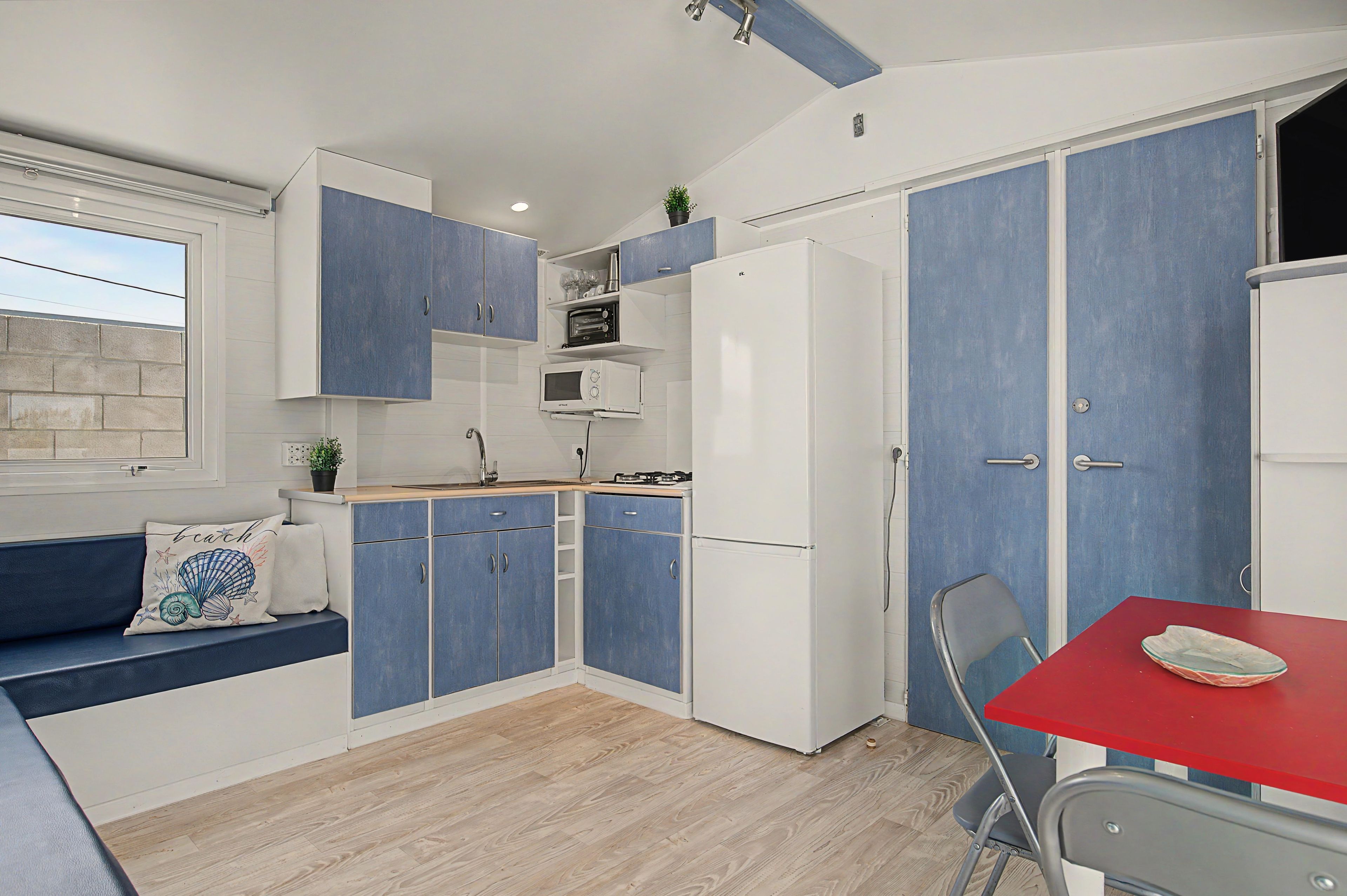 A compact kitchen with blue and white cabinetry, a microwave, a refrigerator, and a dining area with a red table.