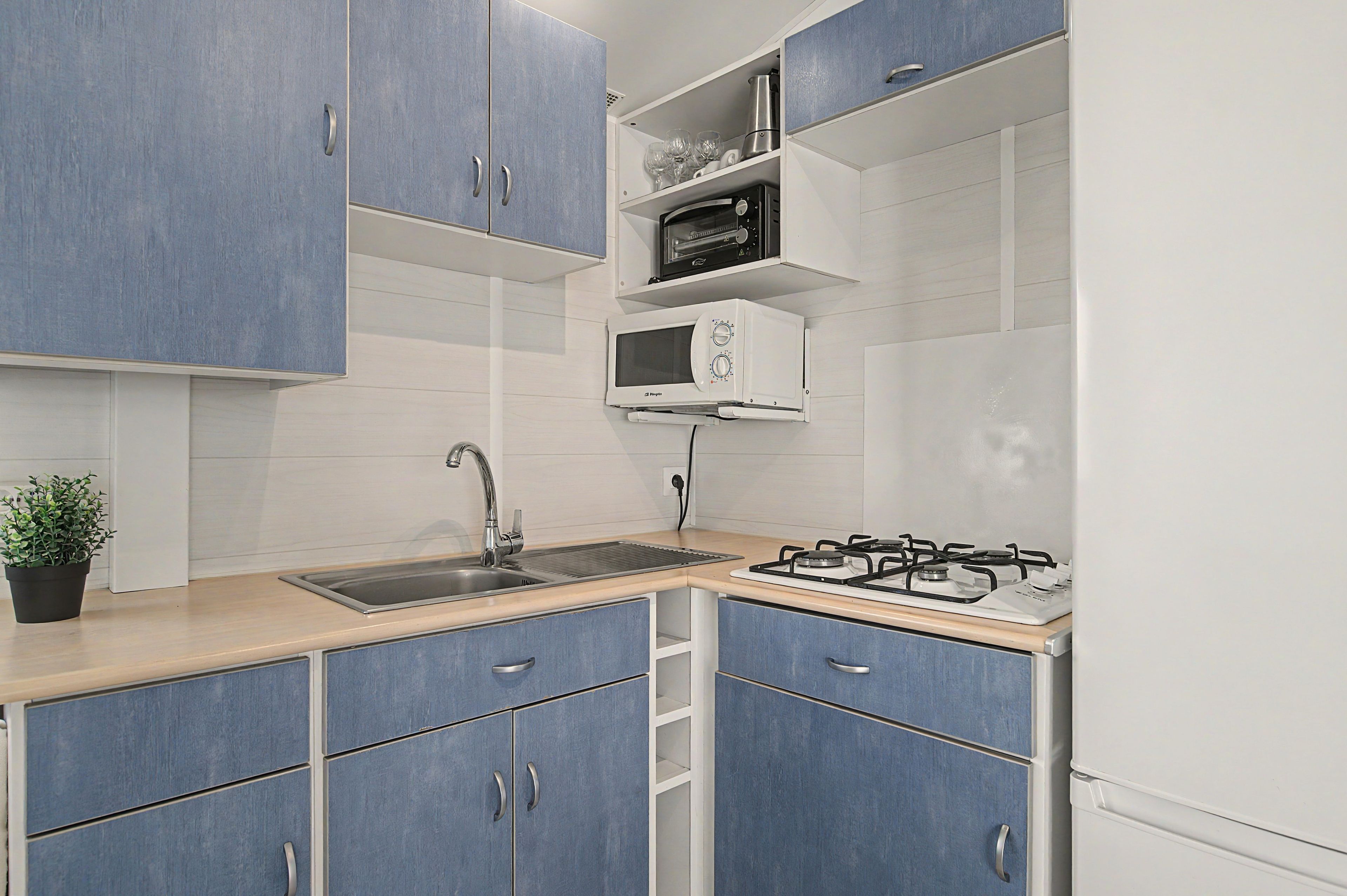 Une cuisine avec des meubles bleus, un évier en acier inoxydable, un four à micro-ondes et une cuisinière à gaz.