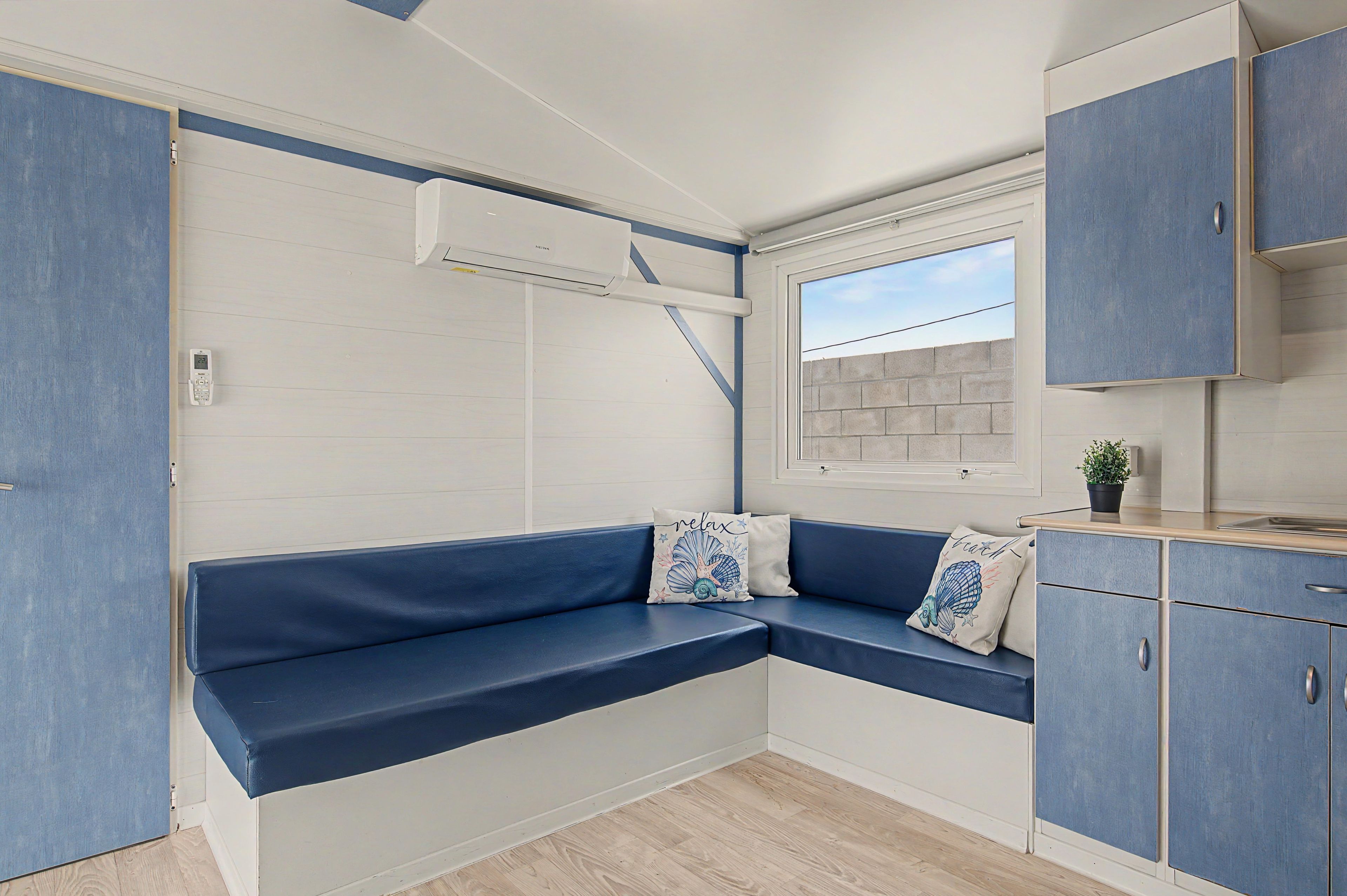 Een compacte kitchenette met een ingebouwde kookplaat, een raam met uitzicht en een blauwe bank met decoratieve kussens.