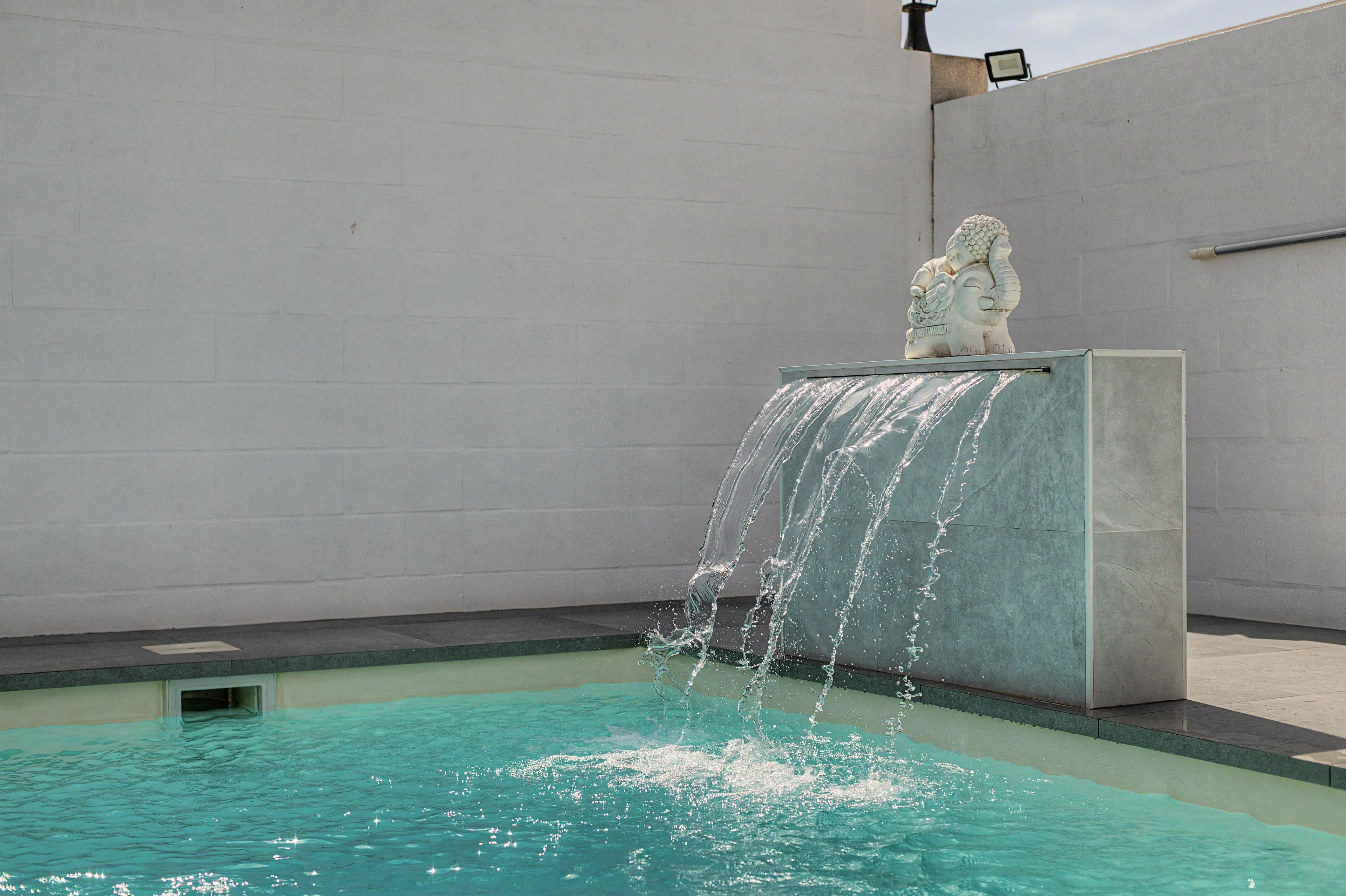 A swimming pool with a waterfall feature and a statue on a pedestal.