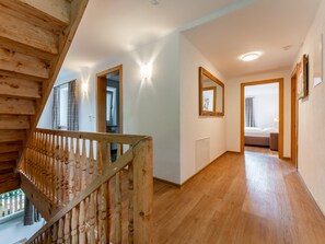 A wooden staircase with a railing, a hallway with a wooden floor, and a bedroom with a bed and a window. - Luxury chalet near Zell am See & Kaprun (Bruck an der Großglocknerstraße)